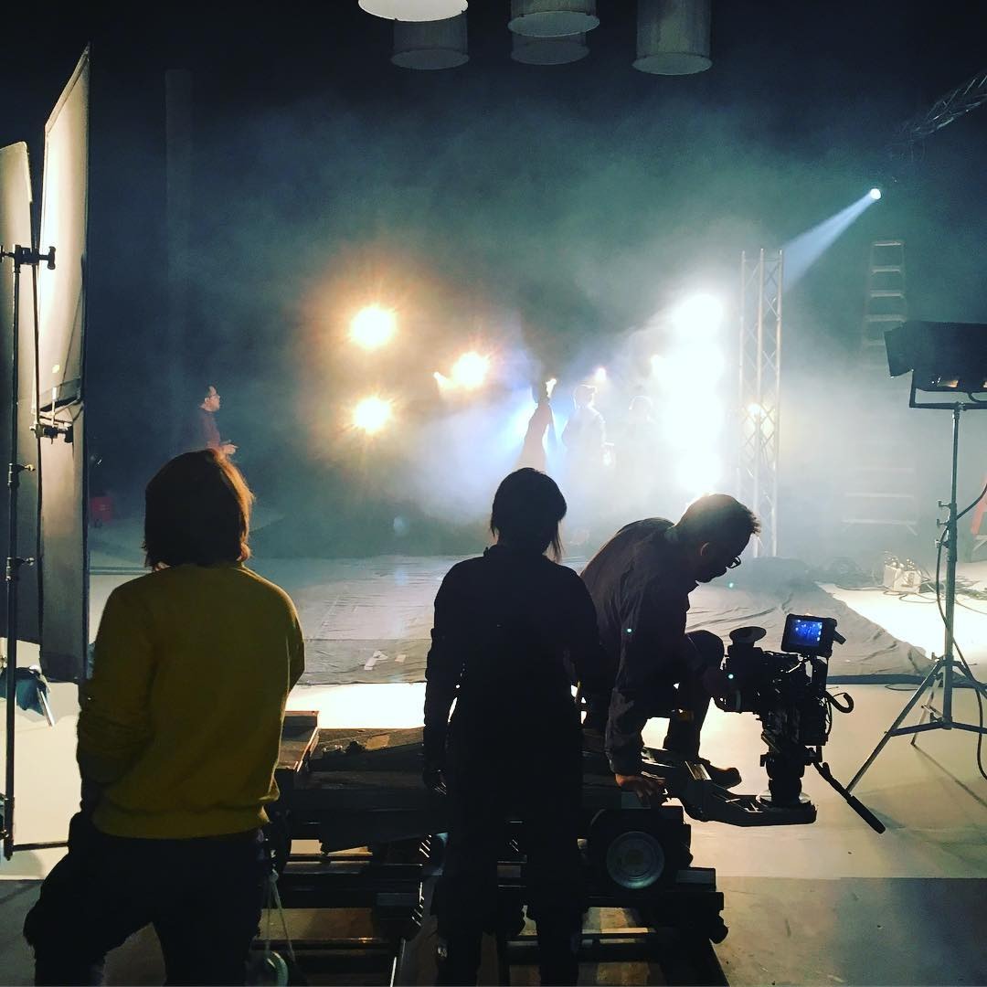 A crew in silhouette on a film set, with stage lights shining through haze.